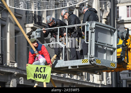 Polizei versucht eine Demonstrantin, die saß auf einem Bambus Struktur der Straße am Oxford Circus, London, während einer Aussterben Rebellion (XR) Klimawandel protest Block ist zu entfernen. Stockfoto