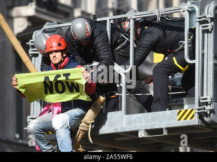 Polizei versucht eine Demonstrantin, die saß auf einem Bambus Struktur der Straße am Oxford Circus, London, während einer Aussterben Rebellion (XR) Klimawandel protest Block ist zu entfernen. Stockfoto