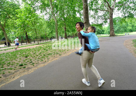 London, England, UK. Mutter ihren Sohn auf dem Rücken im Green Park Stockfoto