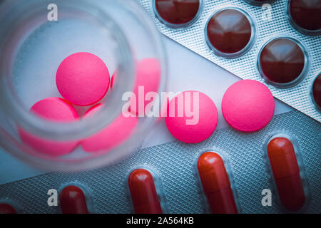 Blisterpackungen mit bunten Tabletten und rosa Pillen sind aus Glas auf einem weißen Hintergrund blau gegossen. Der Blick von oben Stockfoto