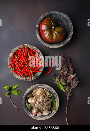 Ansicht von oben von drei rustikale Schüsseln mit Tomaten, Peperoni, Knoblauch und lila Basilikum Stockfoto