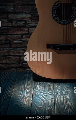 Akustik Gitarre stehend an der Wand durch einen Lichtstrahl beleuchtet. Lichtfleck auf dem Dielenboden Stockfoto