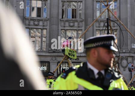 London, Großbritannien. Okt, 2019 18. Ein Klimawandel Aktivist hält ein Schild mit der Aufschrift "Jetzt handeln", wie er in einem behelfsmäßigen Struktur in Oxford Circus sitzt. Credit: Kevin Shalvey/Alamy leben Nachrichten Stockfoto