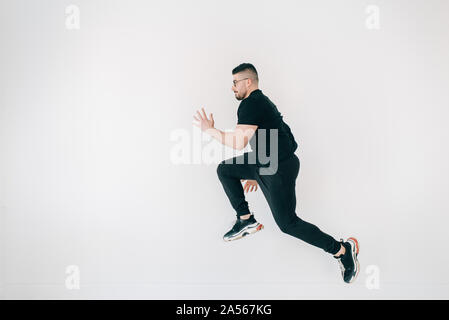 Mann tut hoher Sprung gegen weiße Wand Stockfoto