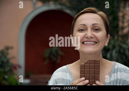 Frau Schokolade essen. Schönes Portrait eines glücklichen Frauen mittleren Alters und lächelnd eine Tafel Schokolade. Stockfoto