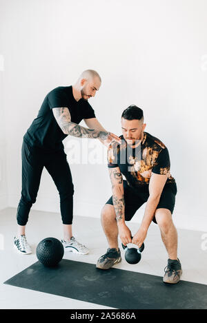 Fitness Instructor lehre Mann tun Hocke mit kettlebell im Studio Stockfoto