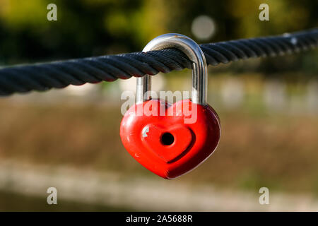 Rotes Herz auf eine metallische Kabel auf der Brücke. Vorhängeschloss in der Form von Herzen an einem Seil. Romantische Konzept. Symbol der Liebe. Stockfoto