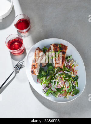 High Key noch Leben mit Gläser Rotwein und die Platte von gestochen scharfer Schweinebauch und asiatischen Salat auf weißem Tabelle, Ansicht von oben Stockfoto