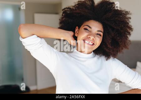 Glückliche junge Frau mit Hand in afro Haar im Schlafzimmer, Kopf und Schulter portrait Stockfoto