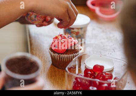 Hand fallen bunte Streusel auf Cupcake Stockfoto