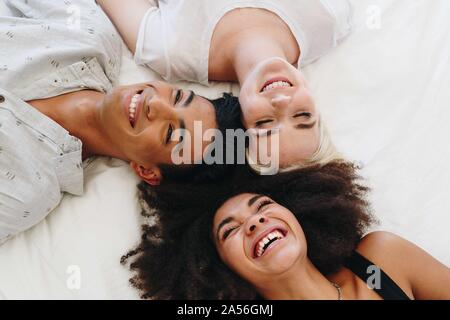 Junger Mann und zwei weibliche Freunde liegend auf Bett lachen, Ansicht von oben Stockfoto