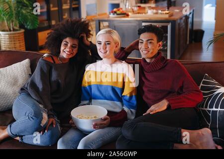 Junge Menschen und junge weibliche Freunde Fernsehen auf Wohnzimmer Sofa mit Schüssel Popcorn Stockfoto
