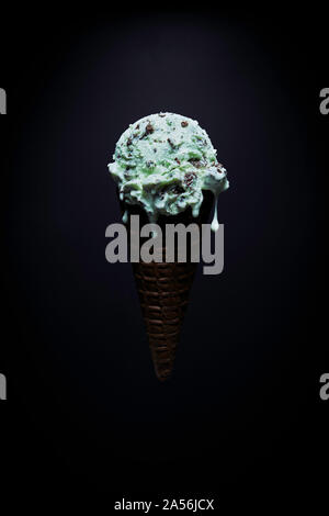 Chocolate Chip mint Eiscreme Kegel mit geschmolzenem Tröpfchen auf schwarzem Hintergrund Stockfoto