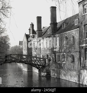 1950er Jahre, historisch, ein Mann auf der so genannten „Mathematical Bridge“ am Queens College, Cambridge University, England, UK, eine Holzbrücke, die die Flusskamera überquert. 1748 von William Etheridge entworfen und im folgenden Jahr von James Essex dem Jüngeren gebaut, wurde es 1905 nach demselben Entwurf umgebaut. Es ist an das Riverside Building angeschlossen, das vermutlich das älteste Gebäude am Fluss ist und um 1460 erbaut wurde. Stockfoto