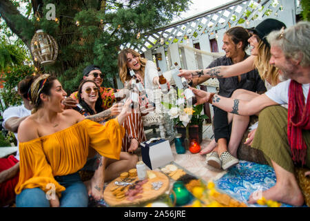 Männliche und weibliche Freunde machen ein Toast mit Flaschenbier auf Gemeinschaftsebene Garden Party Stockfoto