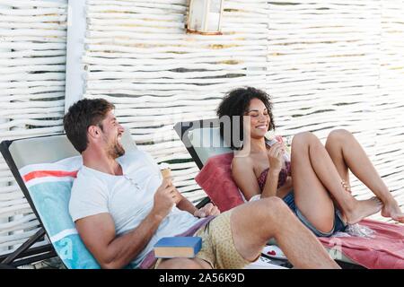 Paar sprechen und genießen Eis Kegel auf Liegestühlen Stockfoto