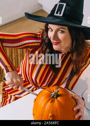 Schöne junge Frau mit schwarzen Hexe hat in ihrer Küche schneiden ein Kürbis für Halloween. Stockfoto