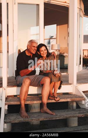 Senior Paar beim Sonnenuntergang auf der Treppe vor Beach House Stockfoto