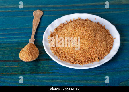 Eine Platte und ein Löffel mit braunem Zucker auf blauem Hintergrund. Stockfoto