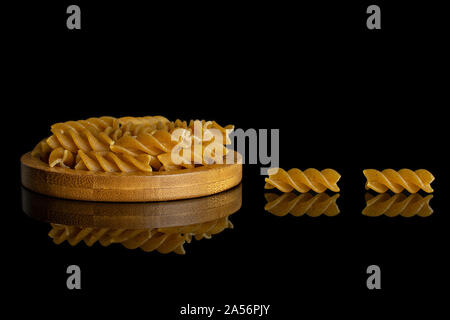 Menge ganz trocken braun Vollkorn fusilli auf Bambus Untersetzer auf schwarzem Glas isoliert Stockfoto