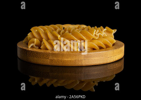 Menge ganz trocken braun Vollkorn fusilli auf Bambus Untersetzer auf schwarzem Glas isoliert Stockfoto