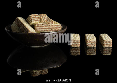 Menge ganze knusprige beige hazelnut Wafers Cookie in dunkle Keramik Schüssel auf schwarzem Glas isoliert Stockfoto