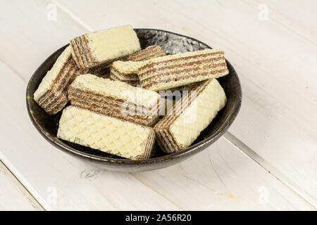 Menge ganze knusprige beige hazelnut Wafers Cookie in dunkle Keramik Schüssel auf weißem Holz Stockfoto