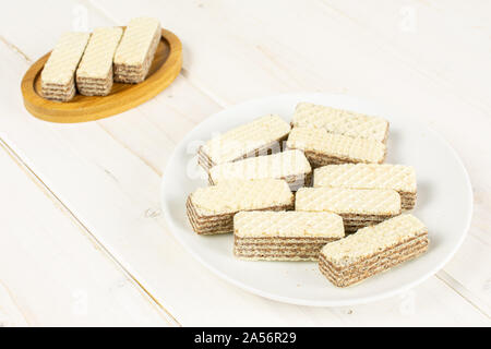 Menge ganze knusprige beige hazelnut Wafers Cookie auf Bambus Untersetzer auf weißer Keramik Platte auf weißem Holz Stockfoto