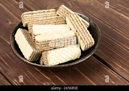 Menge ganze knusprige beige hazelnut Wafers Cookie in dunkle Keramik Schüssel auf braunem Holz Stockfoto