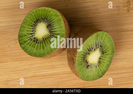 Gruppe von zwei Hälften von exotischen braunen Kiwi flatlay auf hellem Holz. Stockfoto