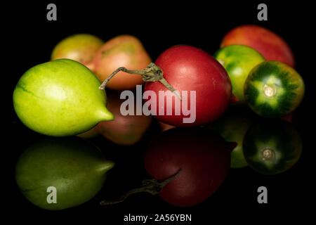 Gruppe von Sieben ganze frische Tomaten de Barao auf schwarzem Glas isoliert Stockfoto