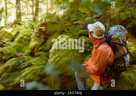 Frau in orange Jacke sitzen auf dem Felsen bedeckt mit der Moss Stockfoto