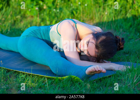 Schöne junge Frau zu tun stretching Übung auf grünem Gras in einem Feld oder einem Park. Stockfoto