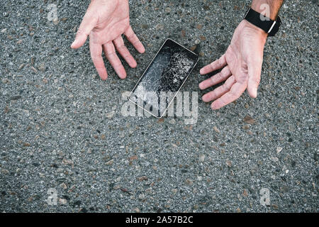 Man ließ das Telefon aus seinen Händen auf dem Asphalt und zertrümmerte den Bildschirm. Kabelbruch im Bildschirm "Telefon" auf der Straße. Die Männer ist unzufrieden. Mobile nicht re Stockfoto