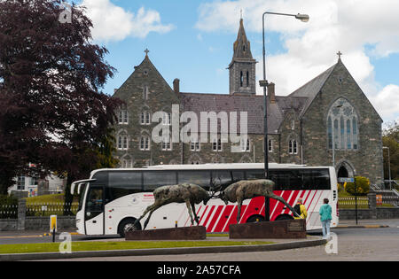 In Killarney, Irland - 14. Juni, 2019: Tour Bus vorbei Kämpfen Roter Hirsch Statue und Kirche Architektur in Killarney, County Kerry Irland. Stockfoto