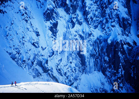 Zwei Bergsteiger auf dem Schneegrat mit der schieren West Angesichts der Aiguille de planen darüber hinaus in der Aiguilles von Chamonix, Frankreich Stockfoto