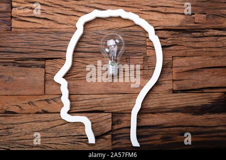 Glühbirne Idee im Kopf Silhouette am Schreibtisch aus Holz Stockfoto