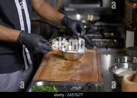 Essen Konzept. Der Küchenchef streusel Mehl frische Austern zum Braten in der Küche. Der Prozess der Spaghetti mit Meeresfrüchten. Stockfoto