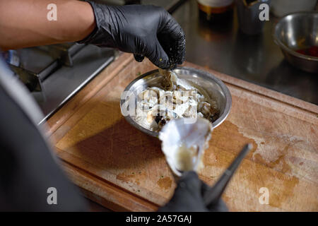 Essen Konzept. Der Küchenchef streusel Mehl frische Austern zum Braten in der Küche. Der Prozess der Spaghetti mit Meeresfrüchten. Stockfoto