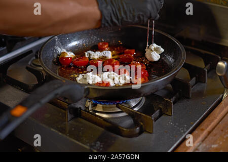 Essen Konzept. Der Küchenchef braten in einer Pfanne die Tomaten und Austern, bereitet die die Teller in die Küche. Der Prozess der Spaghetti mit Meeresfrüchten. Stockfoto