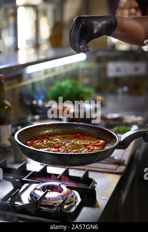 Essen Konzept. Der Küchenchef fügt Gewürzen in einer Pfanne braten die Tomaten und Austern. Der Prozess der Spaghetti mit Meeresfrüchten. Stockfoto