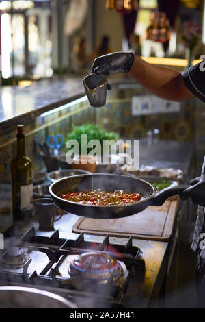 Essen Konzept. Der Küchenchef fügt Gewürzen in einer Pfanne braten die Tomaten und Austern. Der Prozess der Spaghetti mit Meeresfrüchten. Stockfoto