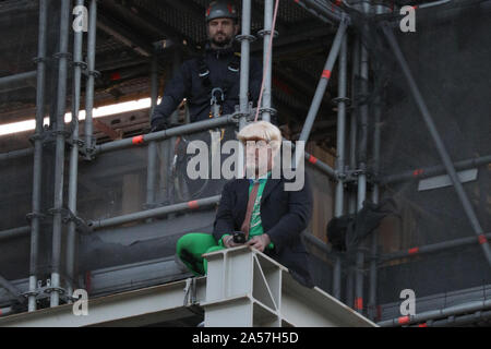 Westminster, London, UK, 18. Okt 2019. Ein Klima Demonstrant vor dem Aussterben Rebellion (XR) hat kletterte Big Ben auf halbem Weg, zwei Banner montiert und sitzt auf einige Gerüste auf der southeatern Ecke der Elizabeth Tower, allgemein bekannt als Big Ben, das Parlamentsgebäude. Polizei Verhandlungsführer Erscheinen auf der Szene gerade über Ihn zu werden. Credit: Imageplotter/Alamy leben Nachrichten Stockfoto