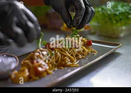 Essen Konzept. Der Koch ist mit frischen Kräutern und Blumen Gerichte im Restaurant eingerichtet. Der Prozess der Herstellung Spaghetti mit Meeresfrüchten. Selektive foc Stockfoto