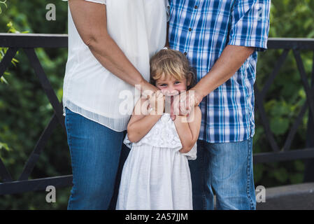 Süße Lächeln 4-yr-old Snuggles zwischen Eltern auf Stahl Brücke Stockfoto