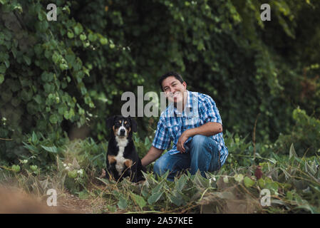 Kniend 40 Jahre alten Mann im blauen Hemd mit Hund im grünen Feld Stockfoto