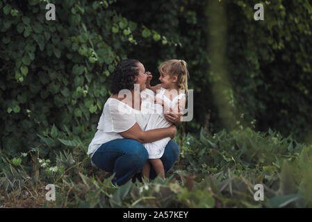 Lachende junge Mädchen die Nase ihr kniend Mutter einklemmen Stockfoto