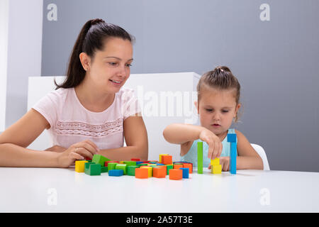 Lächelnd Kindertagesstätte Arbeitnehmer Spielen mit Kind Stapeln Bausteine auf weißem Schreibtisch Stockfoto