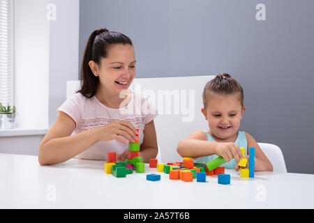 Lächelnd Kindertagesstätte Arbeitnehmer Spielen mit Kind Stapeln Bausteine auf weißem Schreibtisch Stockfoto