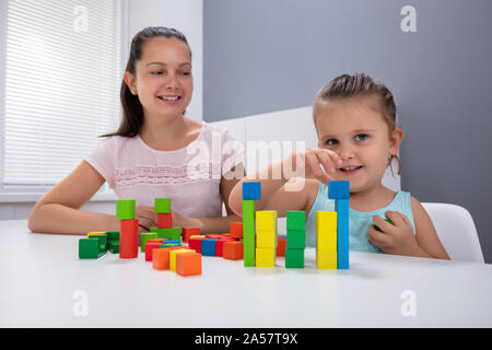 Lächelnd Kindertagesstätte Arbeitnehmer Spielen mit Kind Stapeln Bausteine auf weißem Schreibtisch Stockfoto